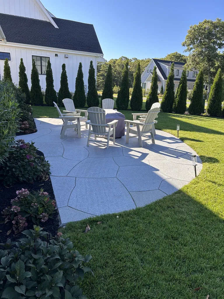 Fire pit seating on a curved stone patio beside the lawn
