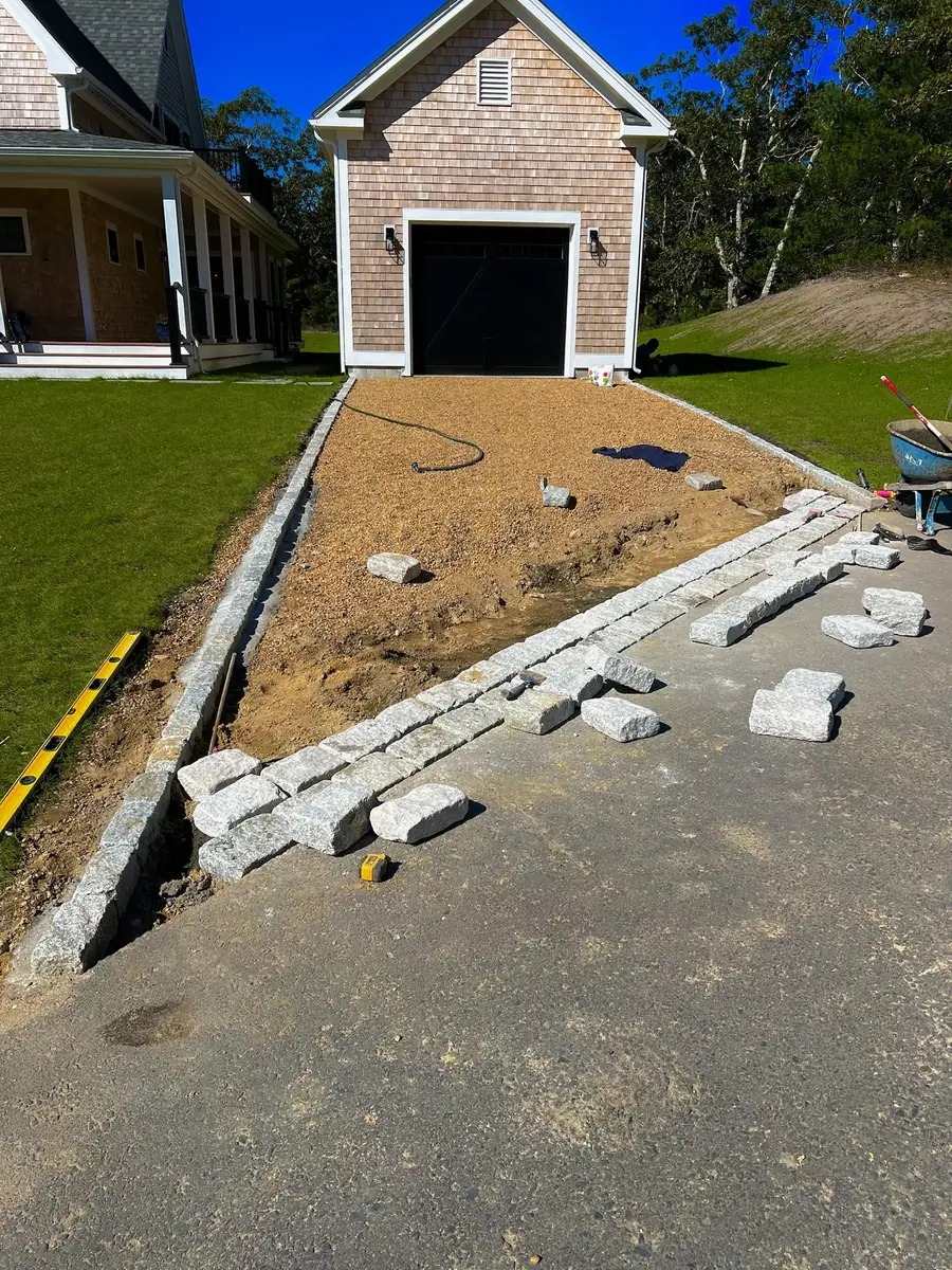 Granite cobblestones being set for a driveway apron and borders at a garage