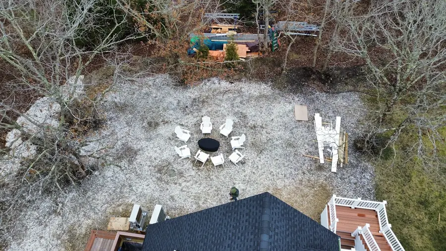 Aerial view of a stone fire ring with Adirondack chairs in a crushed stone area behind a house