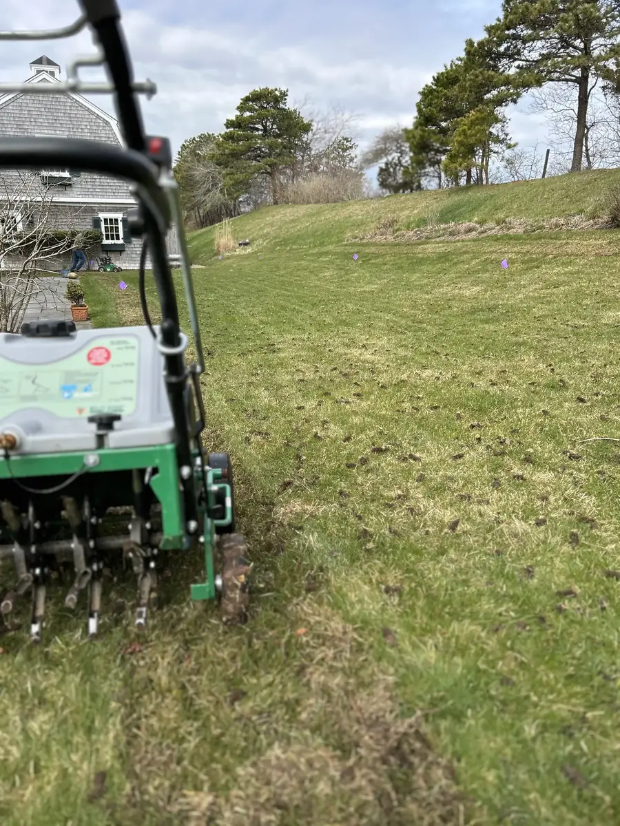 Core aerator working a lawn beside a house