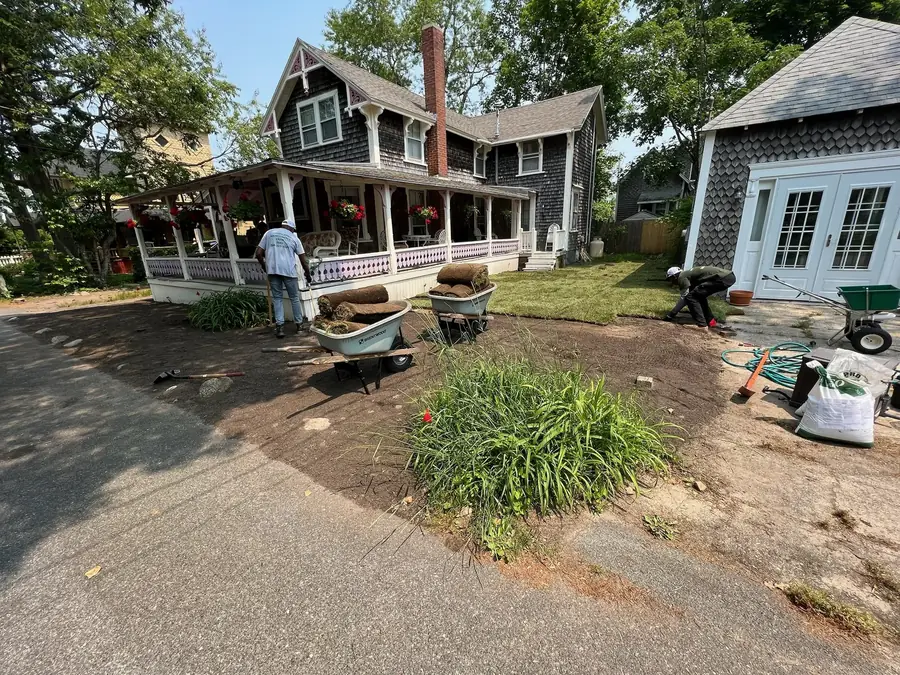 Crew laying sod rolls in front of a shingled cottage