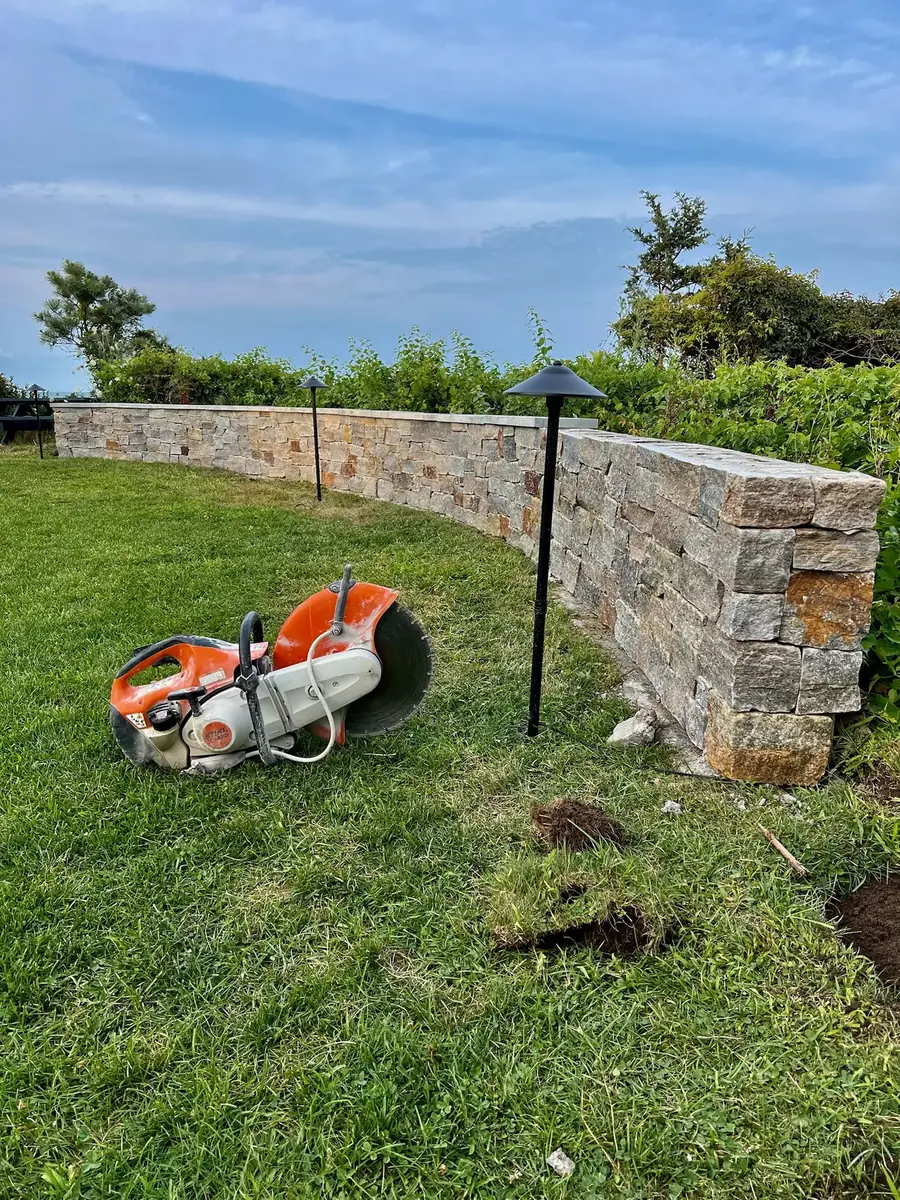 Low-voltage path light installed beside a curved stone veneer wall above the water