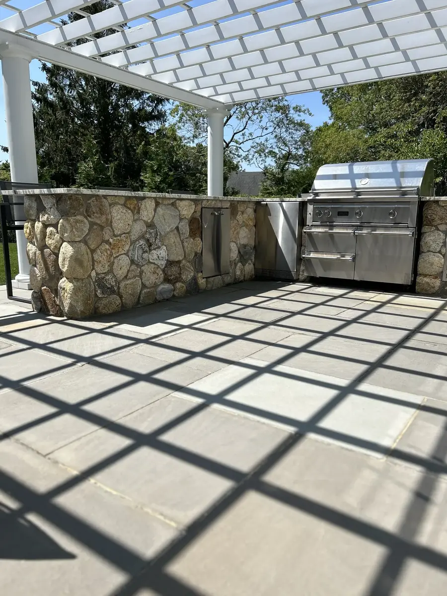 Built-in stainless grill set into a fieldstone kitchen under a pergola