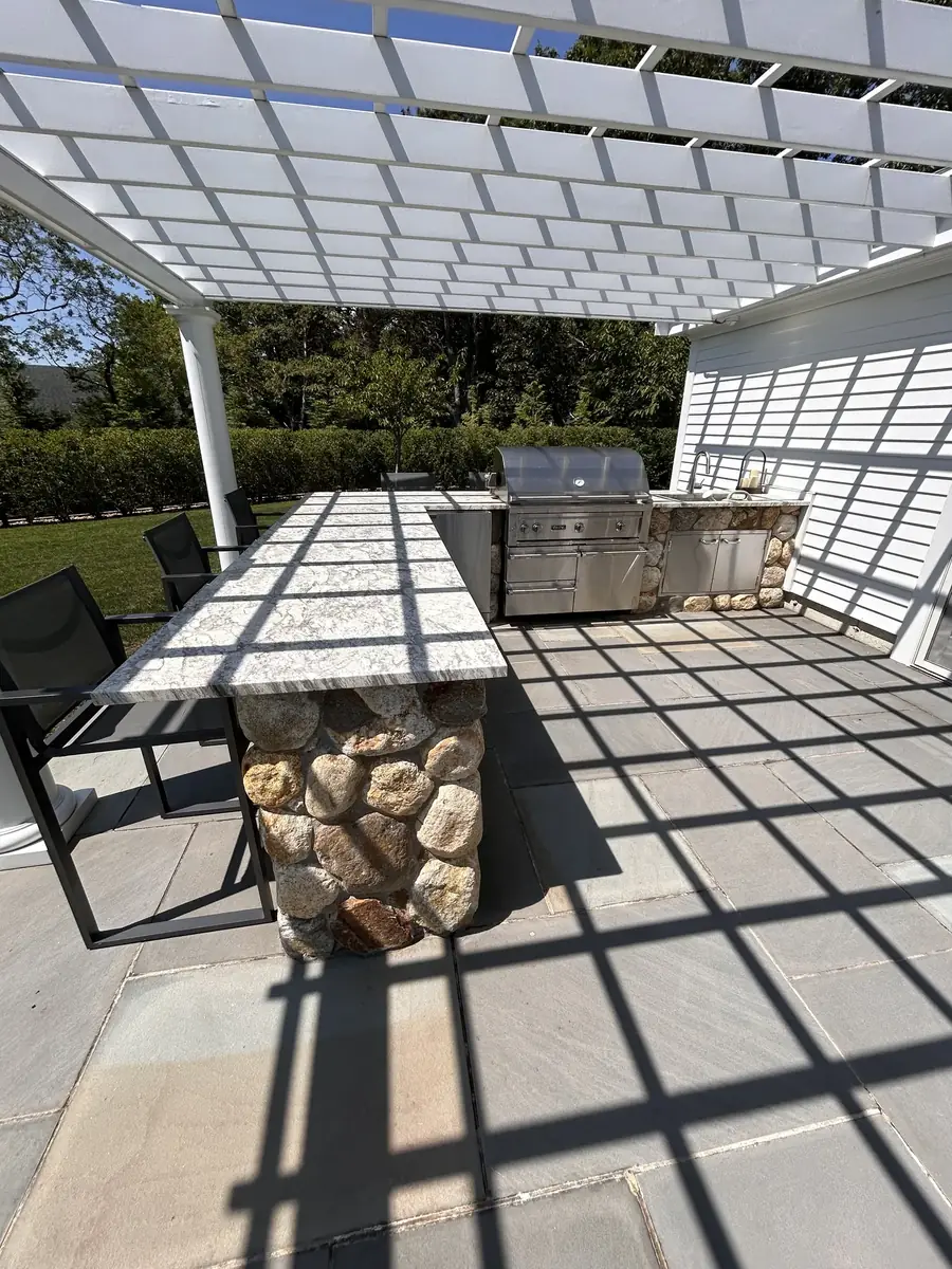Outdoor kitchen with a fieldstone bar and built-in grill under a white pergola