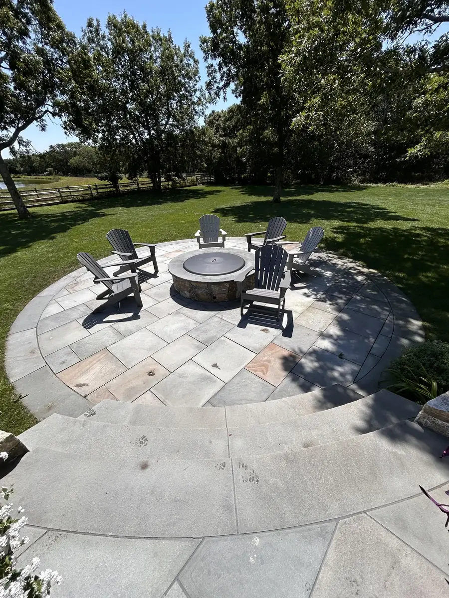 Circular bluestone patio with a round fire pit and Adirondack chairs