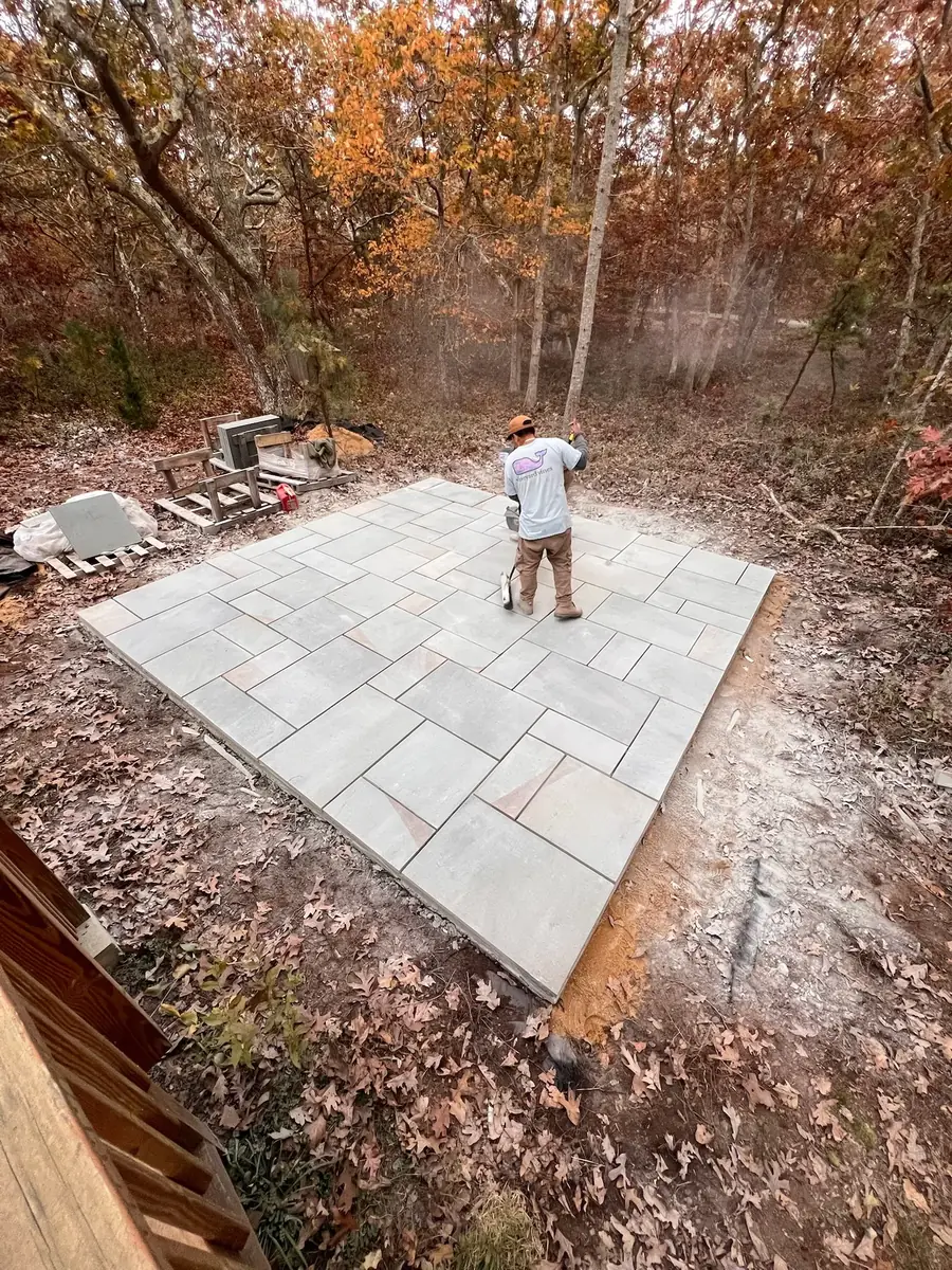 Crew laying out pattern bluestone for a patio on a wooded lot in fall