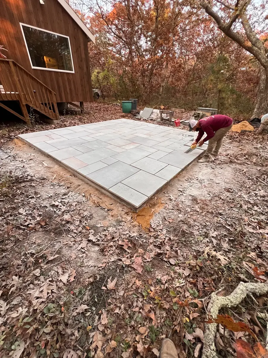 Crew member pointing the joints of a new bluestone patio beside a cedar-sided house