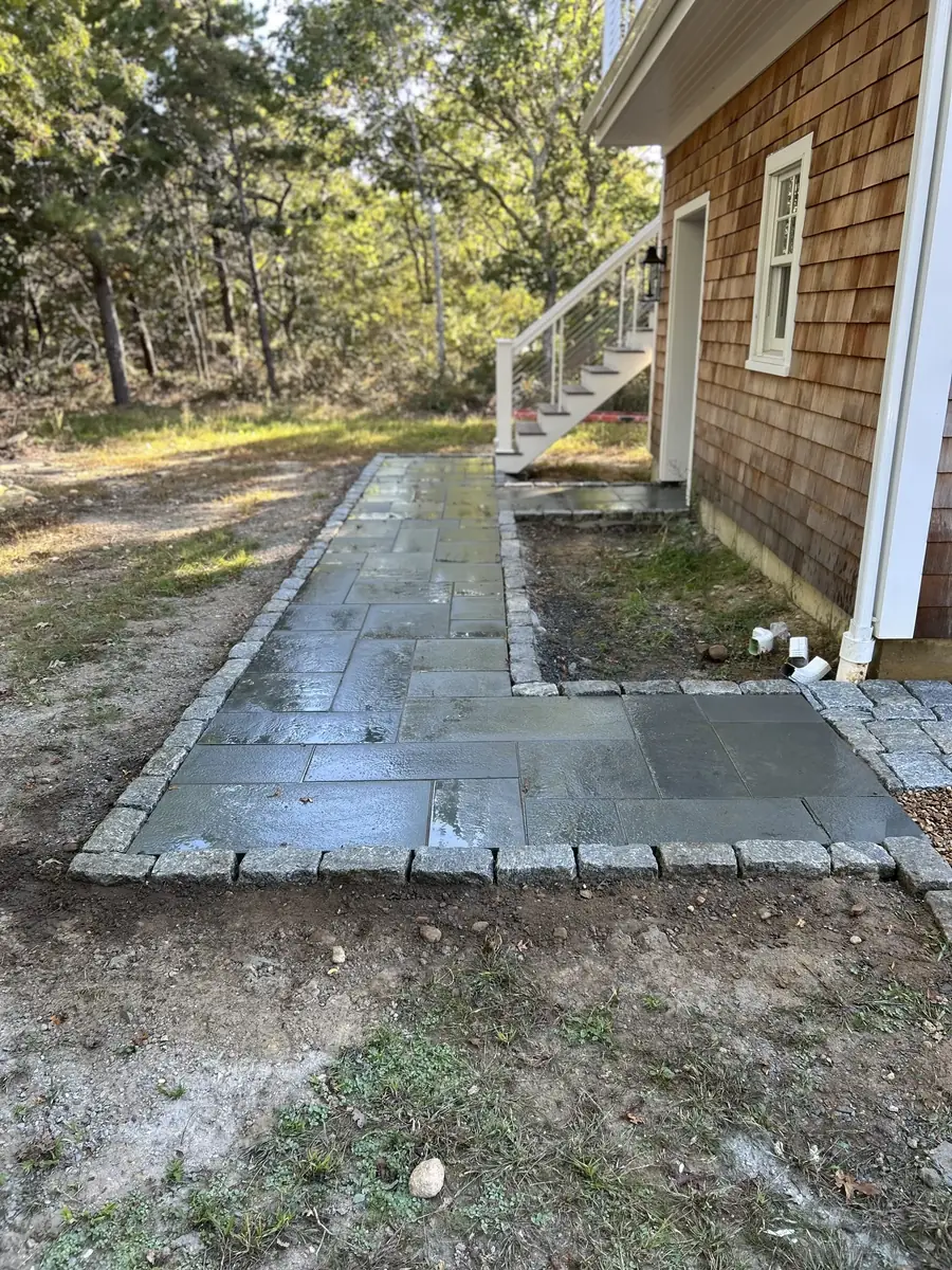 Wet bluestone path with a cobblestone border leading to a side entry