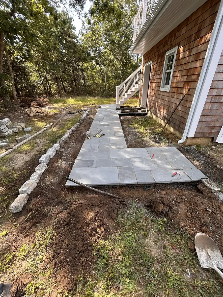 Bluestone walkway being installed with a granite cobblestone border along a shingled house
