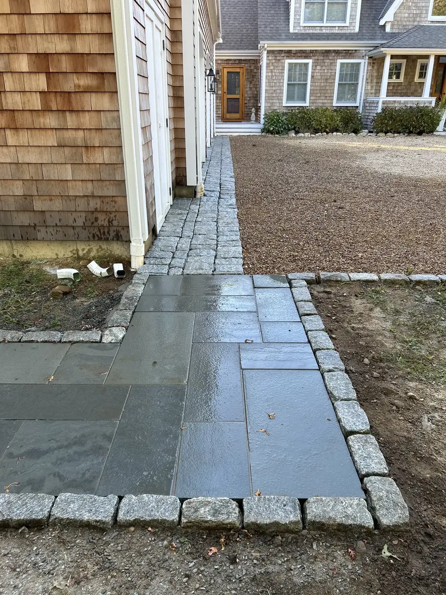 Finished bluestone walkway with a granite cobblestone edge beside a shingled house