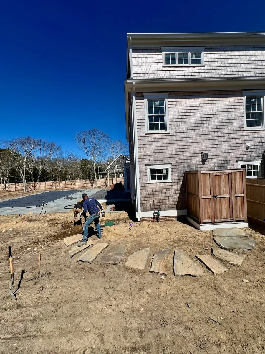 Crew member setting stepping stones in prepared soil beside a shingled house