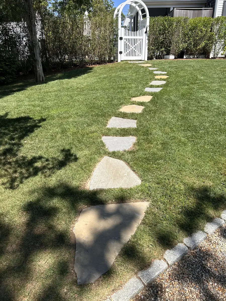 Finished stepping stone path through a green lawn to a white garden arbor