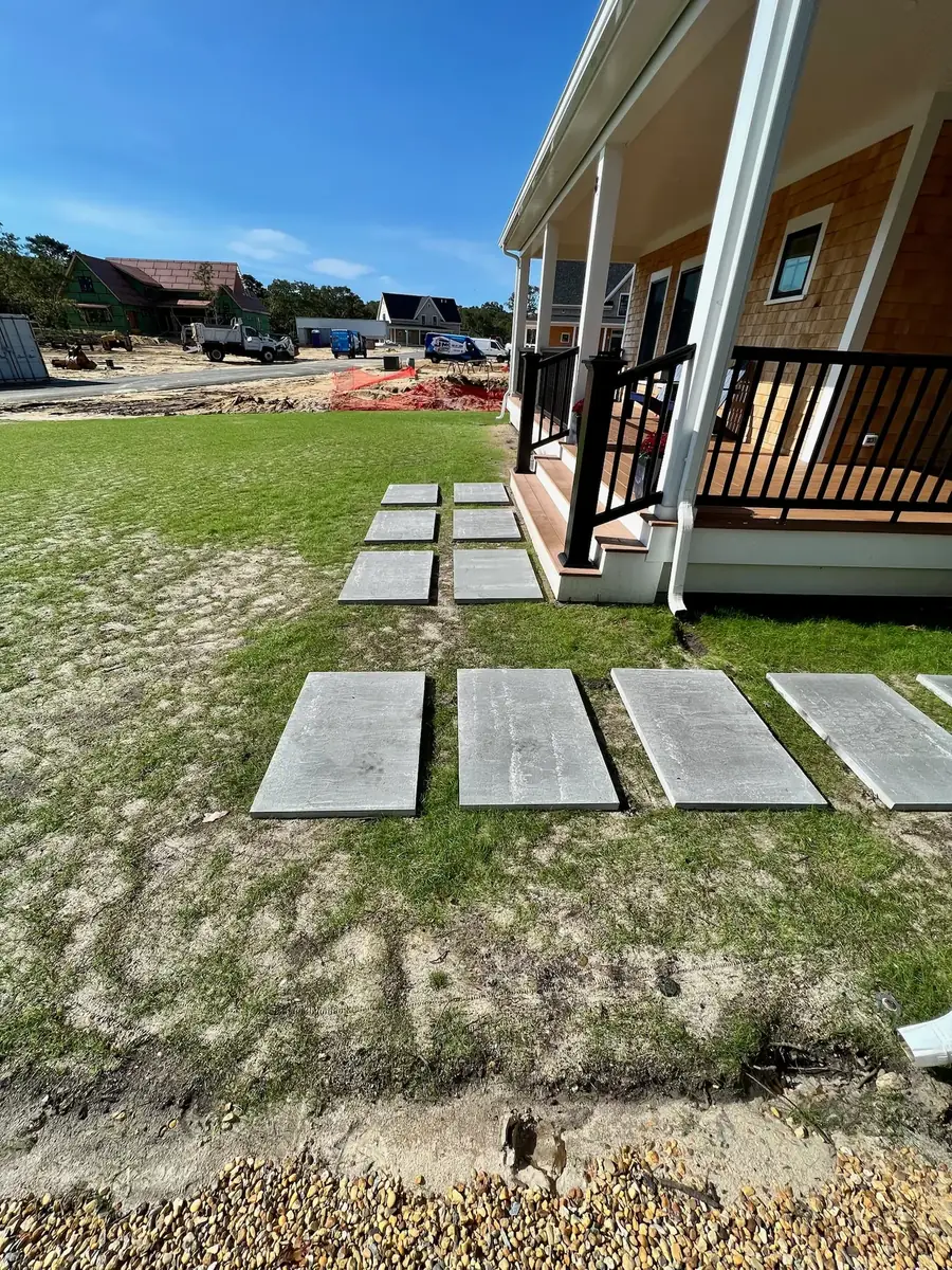 Rectangular stepping stones laid out across a lawn beside a porch before setting