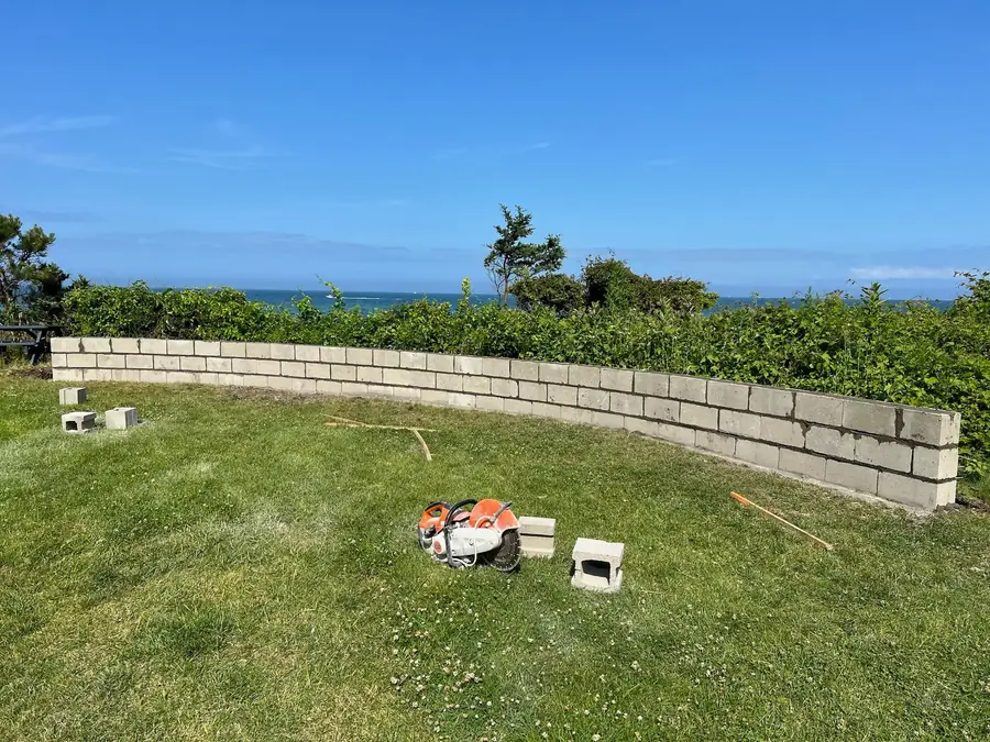 Curved concrete block retaining wall core being built on a lawn above the ocean