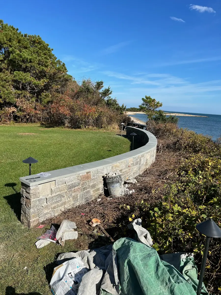 Finished curved stone veneer retaining wall with a stone cap and path lights above the ocean