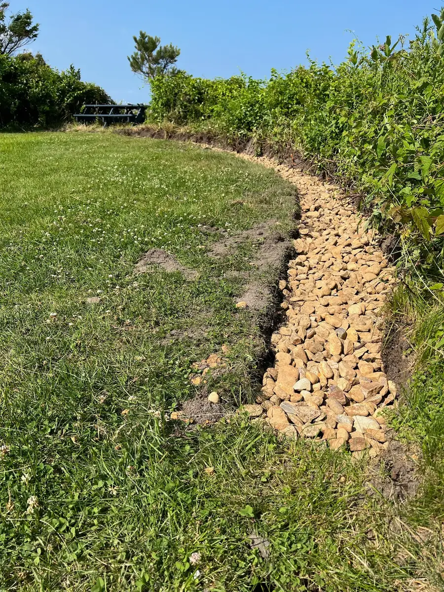 Curved trench filled with crushed stone for a retaining wall footing along a coastal lawn