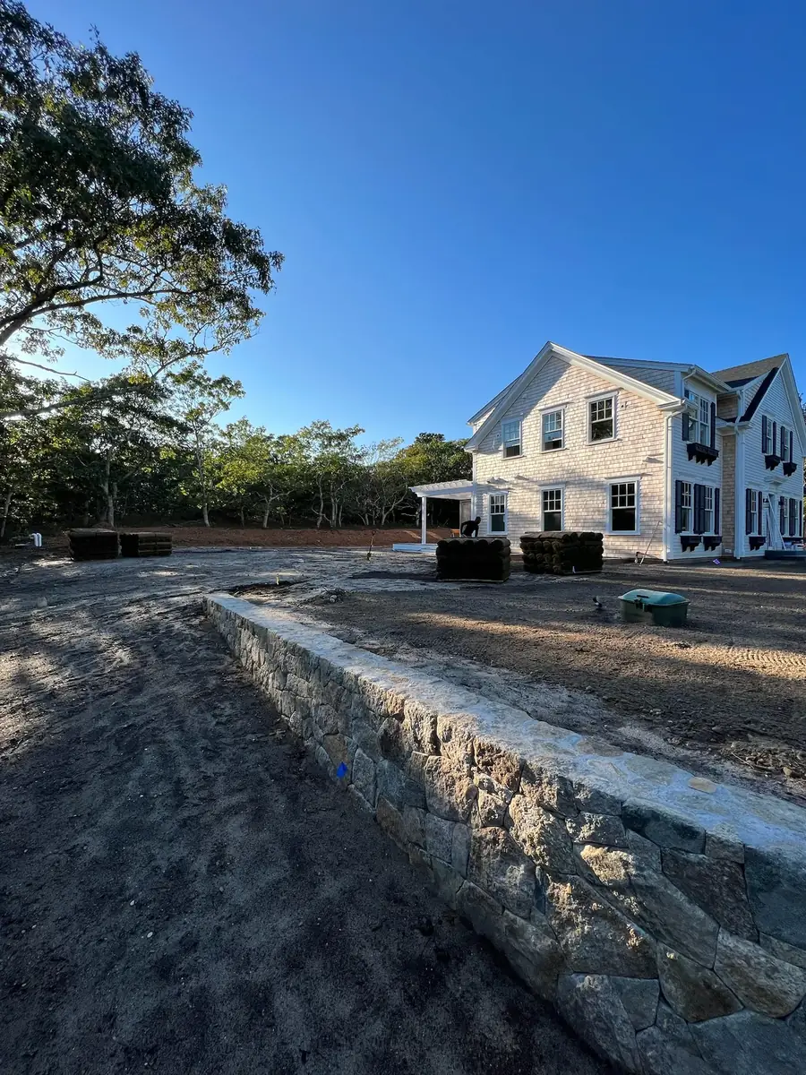 Curved fieldstone retaining wall creating a raised terrace at a new shingled home
