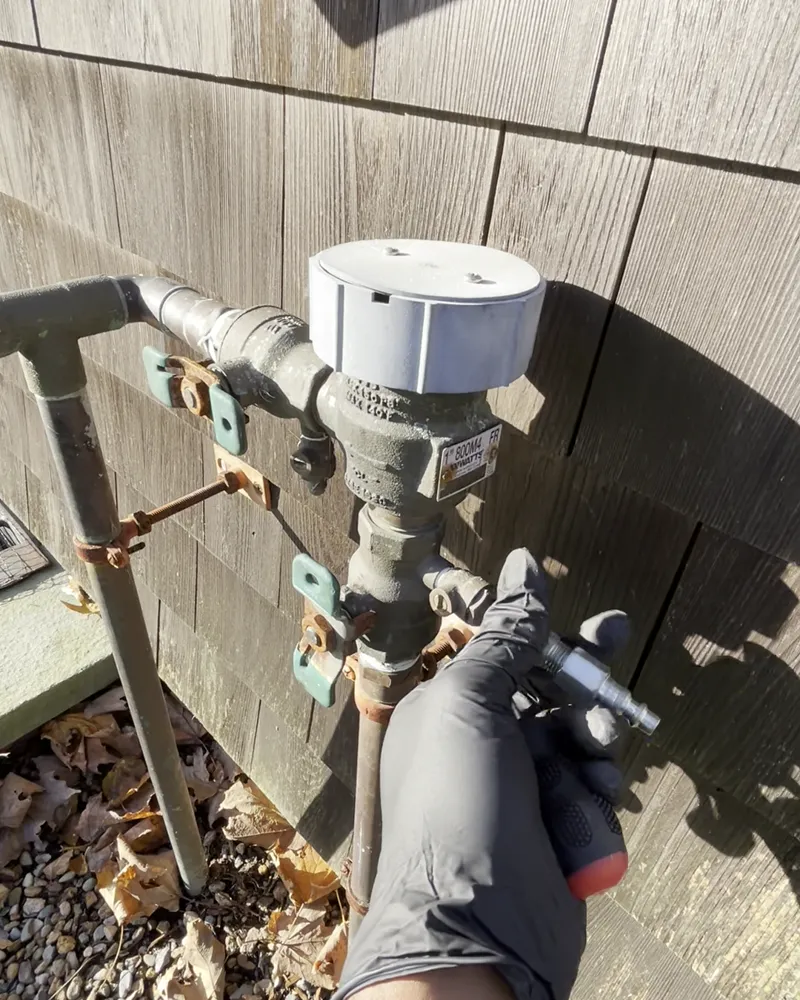 Crew member with a gloved hand at an irrigation backflow preventer on the side of a house