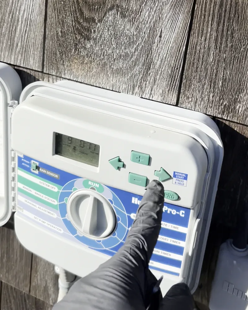 Gloved finger on the buttons of a wall-mounted Hunter irrigation controller