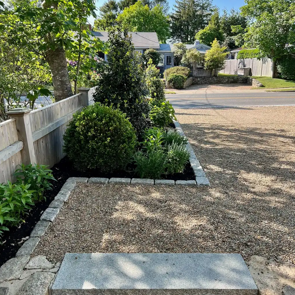 Boxwood and perennials in a granite-edged bed beside a gravel drive