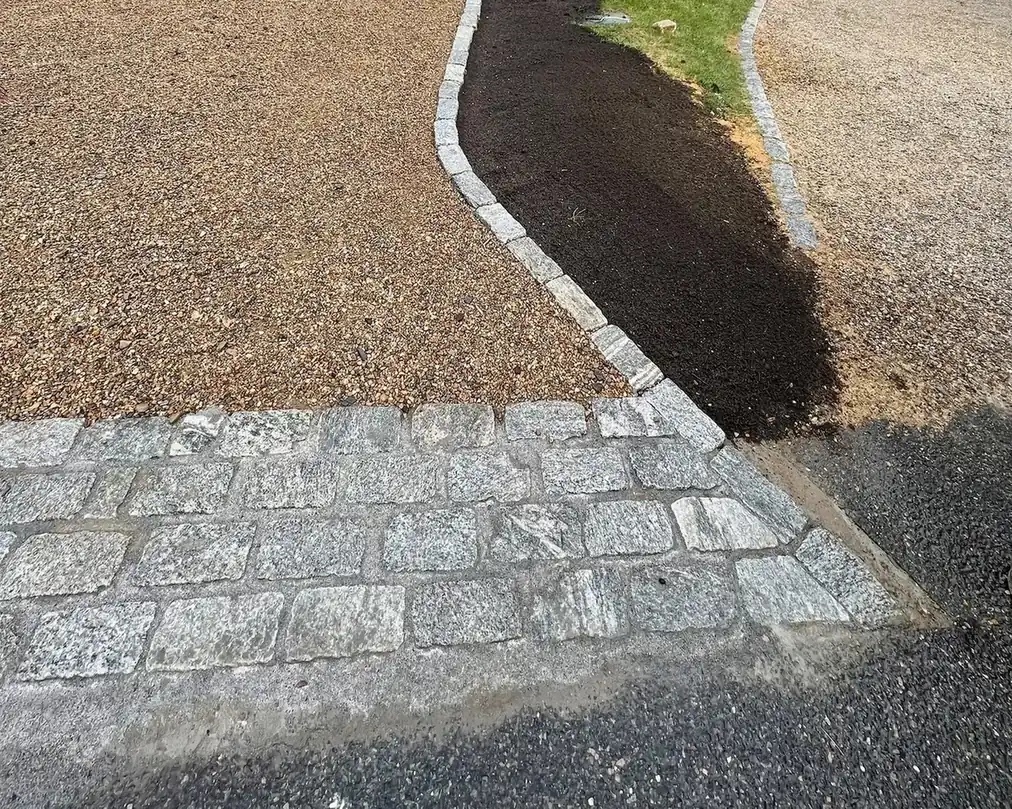 Finished granite cobblestone apron and curb row beside fresh topsoil