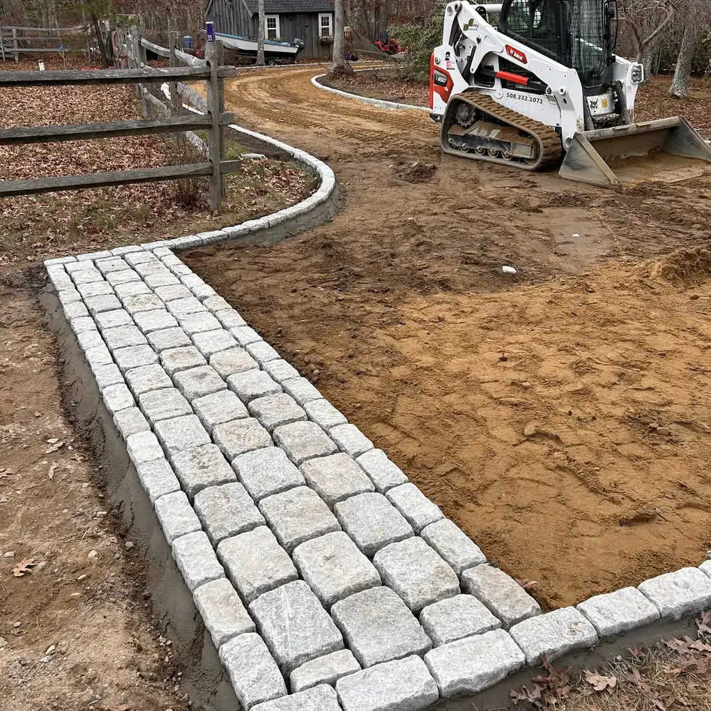 Granite cobblestone band and curved curb row beside a fresh driveway base