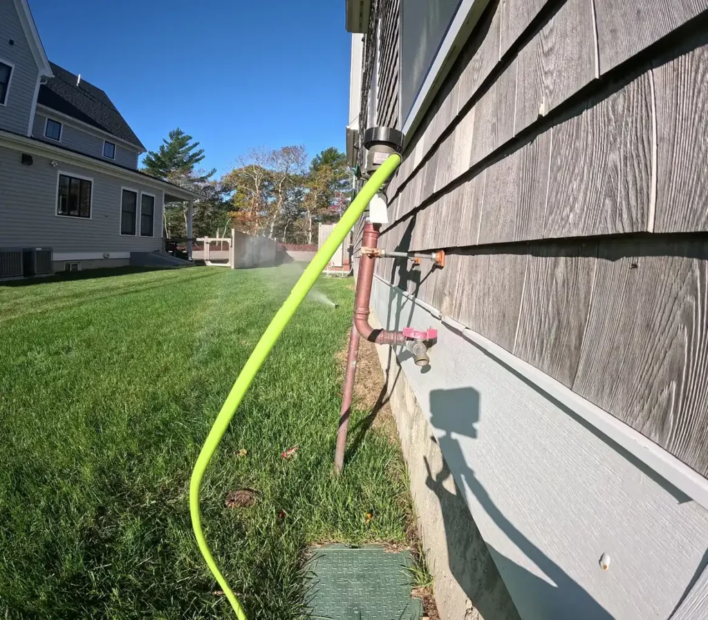 Green air hose connected to the irrigation pipe at a shingled house