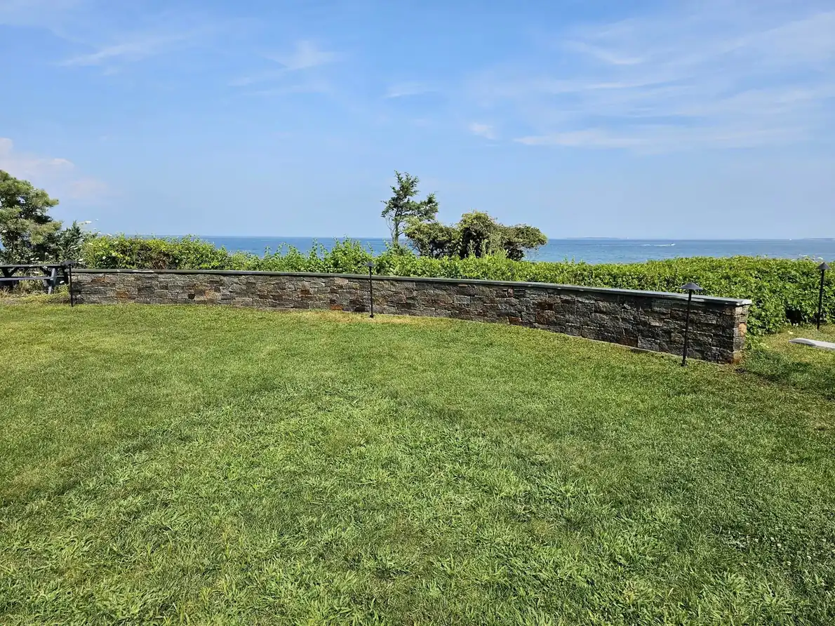 Oceanfront lawn with a low stone wall and coastal shrubs